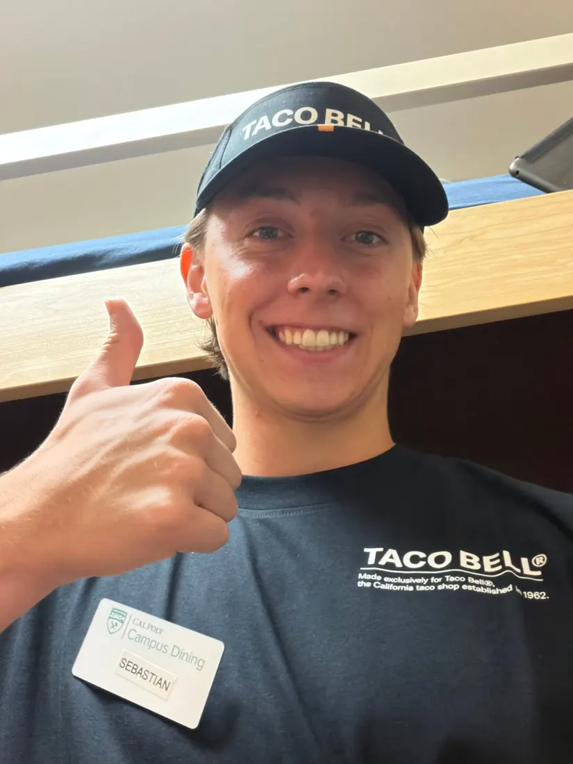 Sebastian in a Taco Bell uniform and cap giving a thumbs up